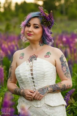 portrait of sensual attractive tattoo bride with multi-colored hair and wreath of flowers in lupines field